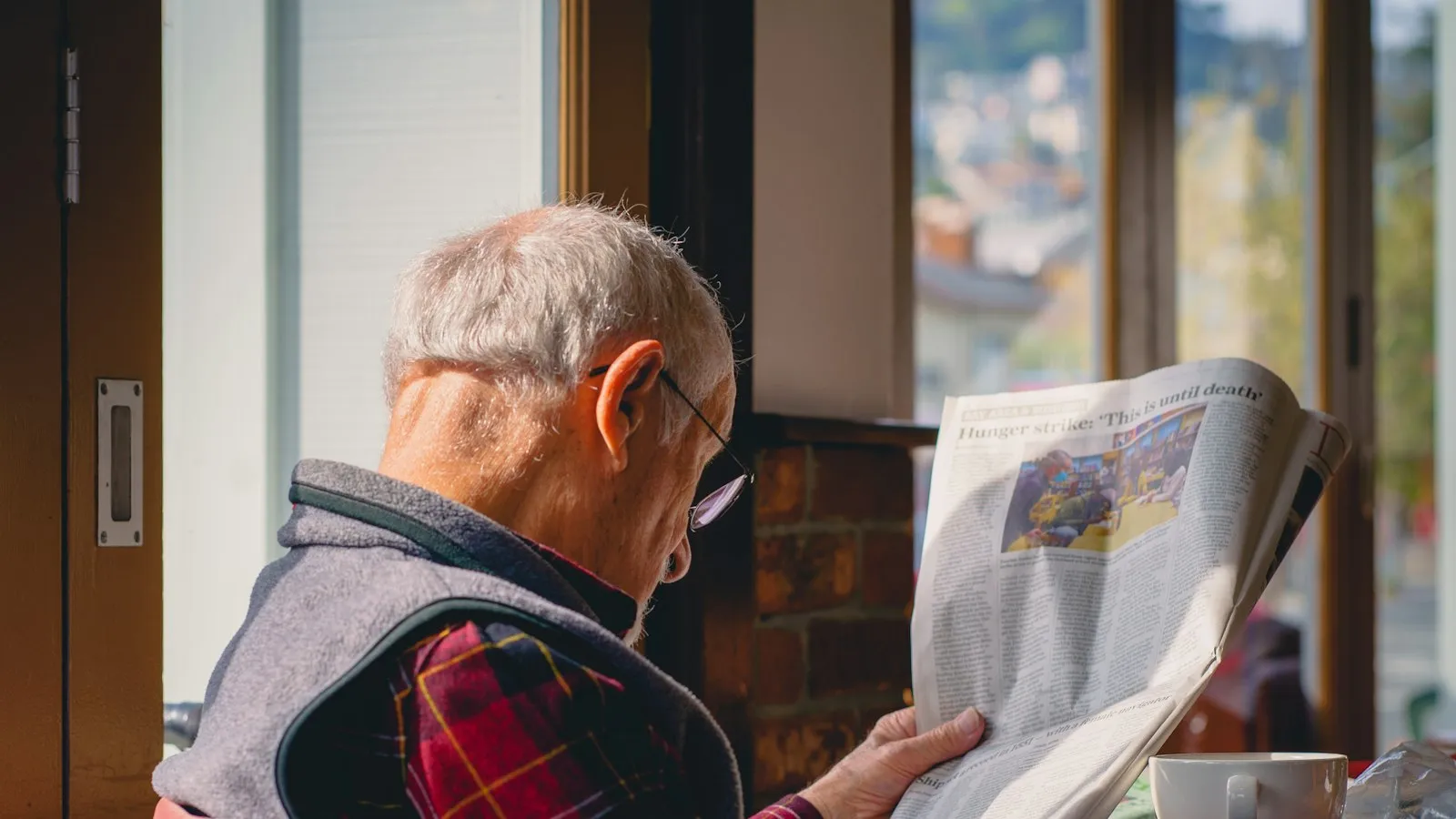 Homem idoso lendo jornal perto da janela